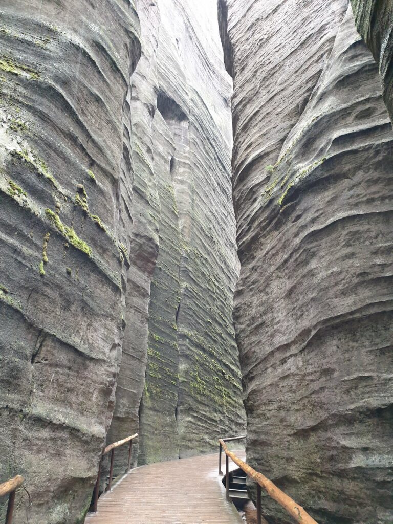 Wąski, zacieniony korytarz między wysokimi skałami z piaskowca w rezerwacie Adršpach w Czechach.