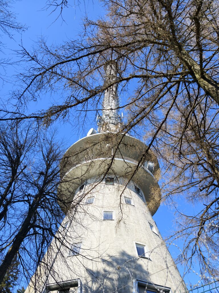 Wysoka, stalowa wieża radiowo-telewizyjna górująca nad drzewami na szczycie Łysej Góry.