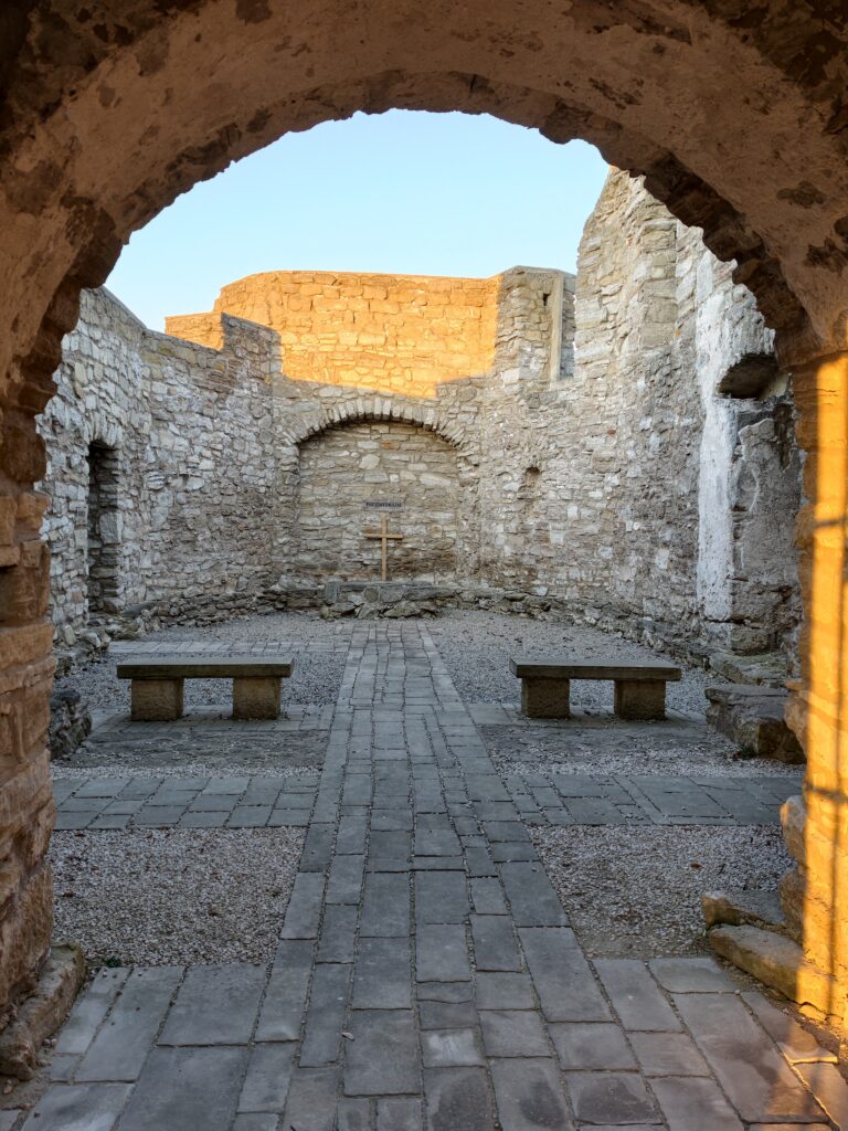 Dziedziniec ruin dawnego szpitala i kościoła Świętego Ducha w Szydłowie – kamienne mury bez dachu, porośnięte trawą wnętrze i błękitne niebo.