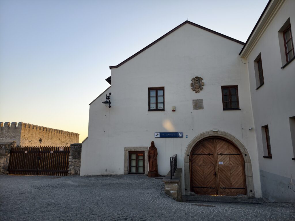 Dziedziniec z ruinami gotyckiego zamku królewskiego i odrestaurowany budynek Skarbczyka w Szydłowie w słoneczny dzień.