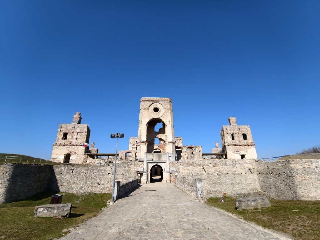 Monumentalna brama wejściowa do Zamku Krzyżtopór w Ujeździe z wyrzeźbionymi symbolami krzyża i topora nad łukiem.
