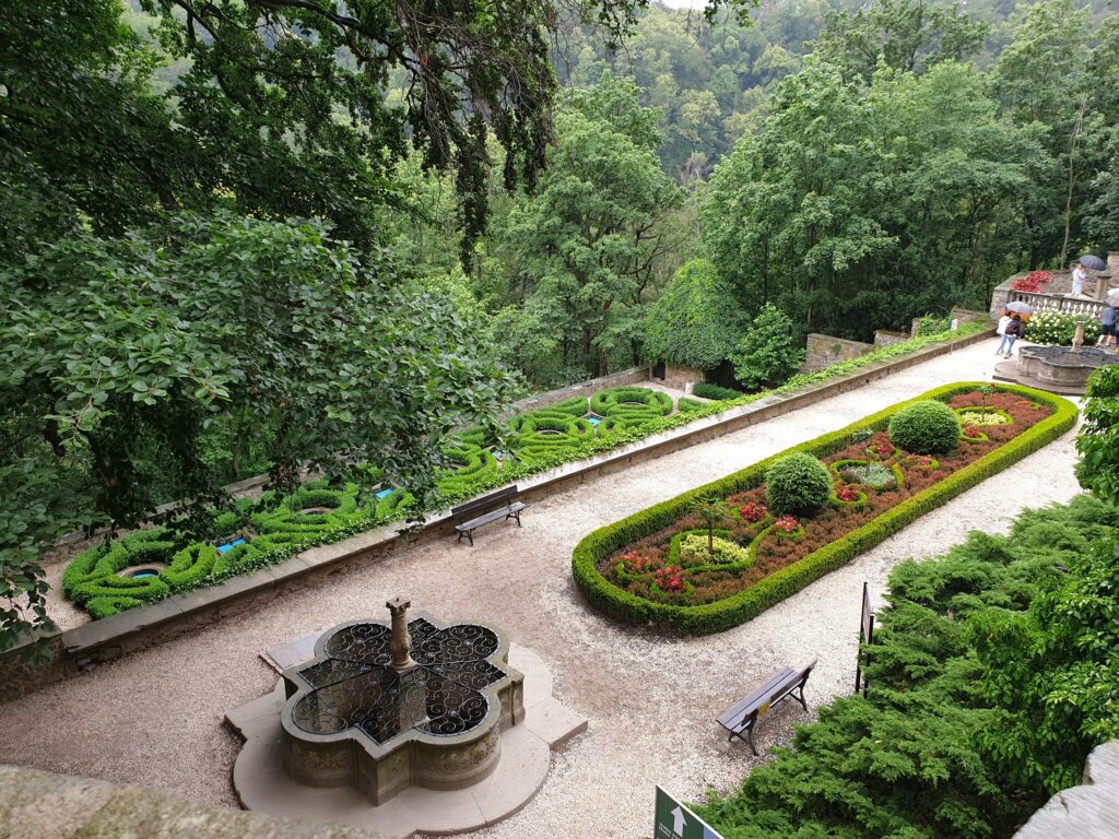 Wypielęgnowane, geometryczne wzory z żywopłotów bukszpanowych w ogrodach tarasowych Zamku Książ w Wałbrzychu. Widok na zalesione wzgórza Książańskiego Parku Krajobrazowego.