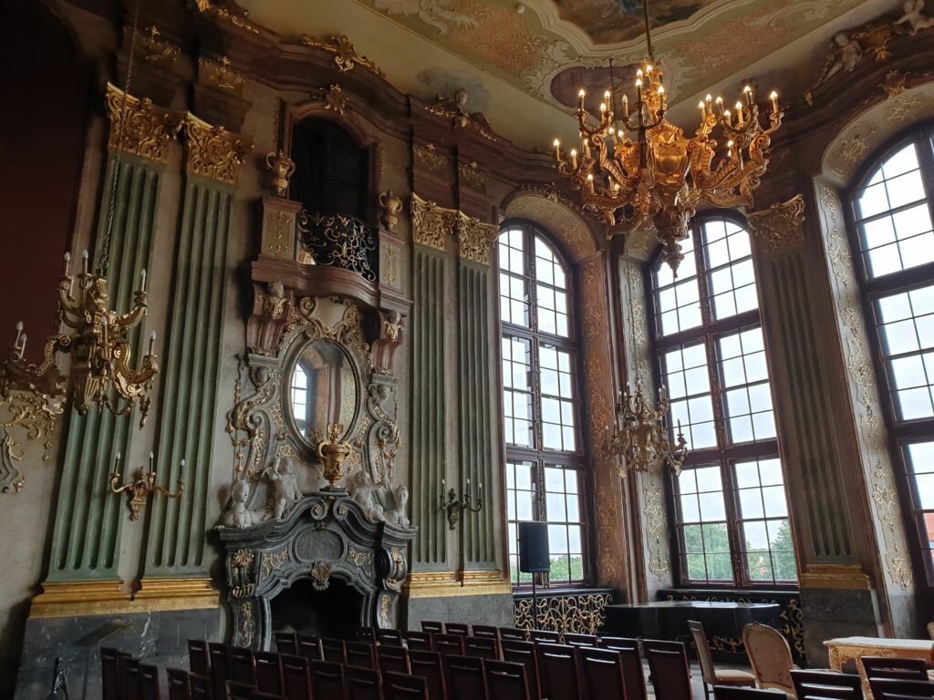 Barokowe wnętrze Sali Maksymiliana w Zamku Książ z bogatymi złoceniami, freskami na suficie i kryształowymi żyrandolami.