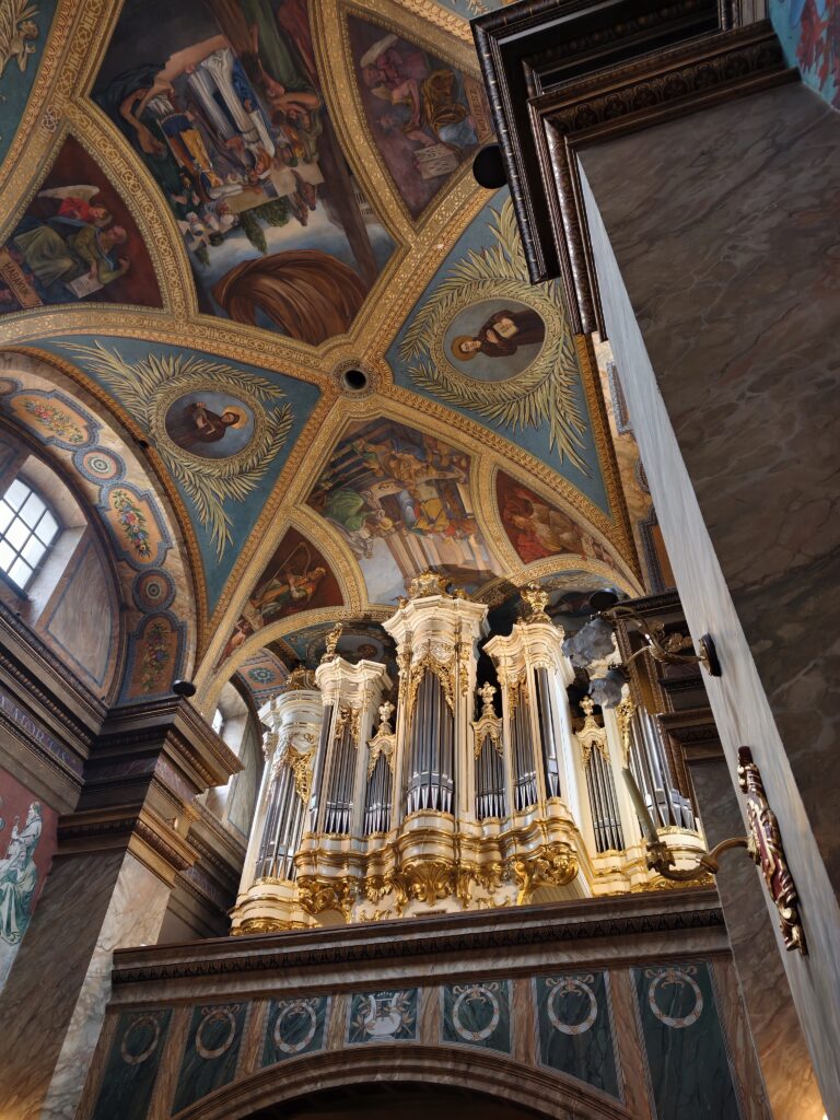 Zbliżenie na bogato zdobione barokowe detale i kolorowe polichromie na sklepieniu Bazyliki Katedralnej w Kielcach.