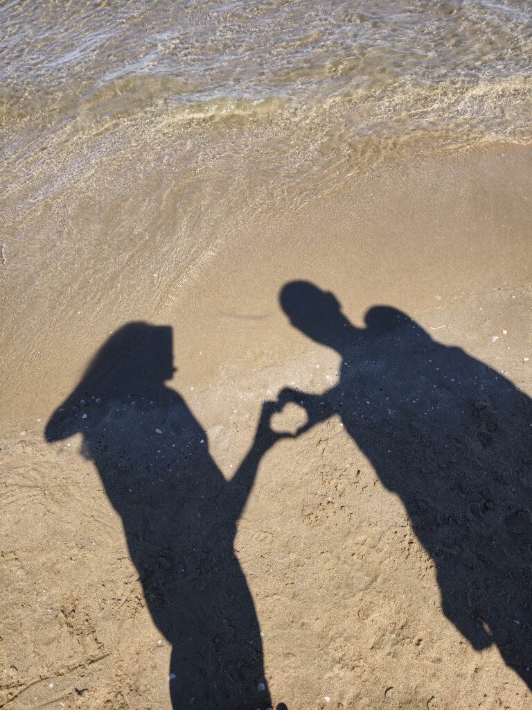 Długie cienie pary pokazujące serce rzucone na złocisty piasek w świetle popołudniowego słońca na plaży Las Arenas w Walencji.