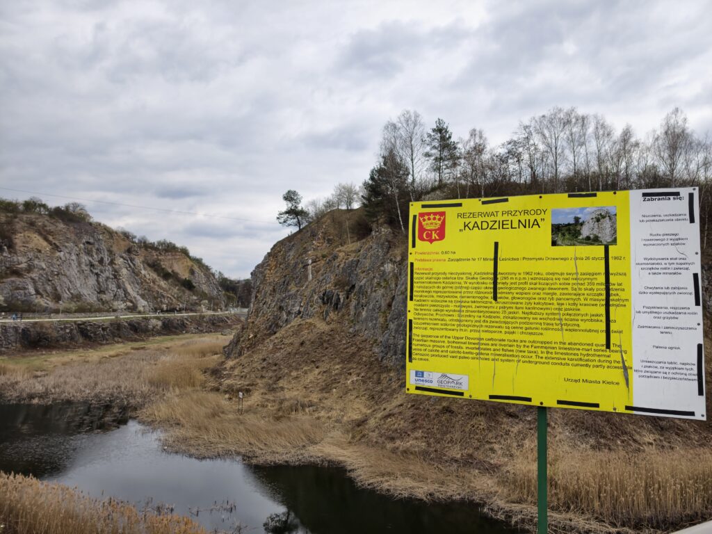 Pionowe, wapienne ściany dawnego kamieniołomu na Kadzielni z tablicą informacyjną.