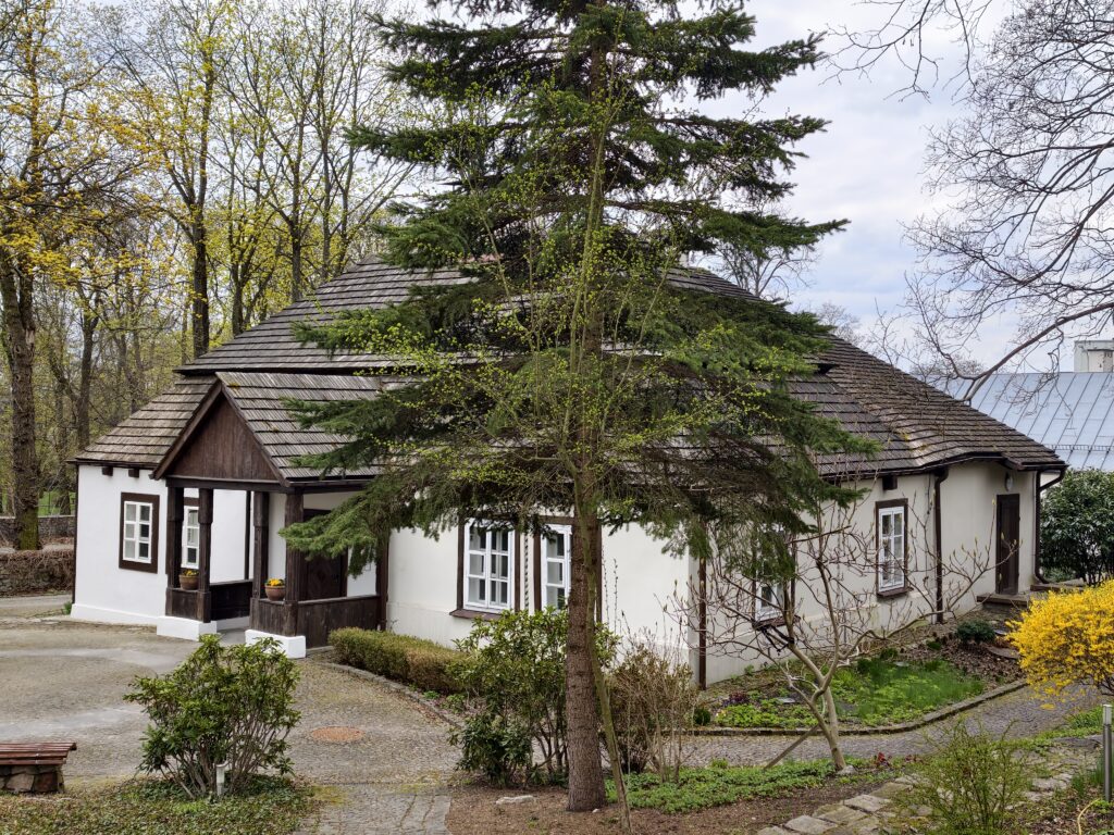 Drewniany, modrzewiowy Dworek Laszczyków z XVIII wieku na tle współczesnej, miejskiej zabudowy Kielc.