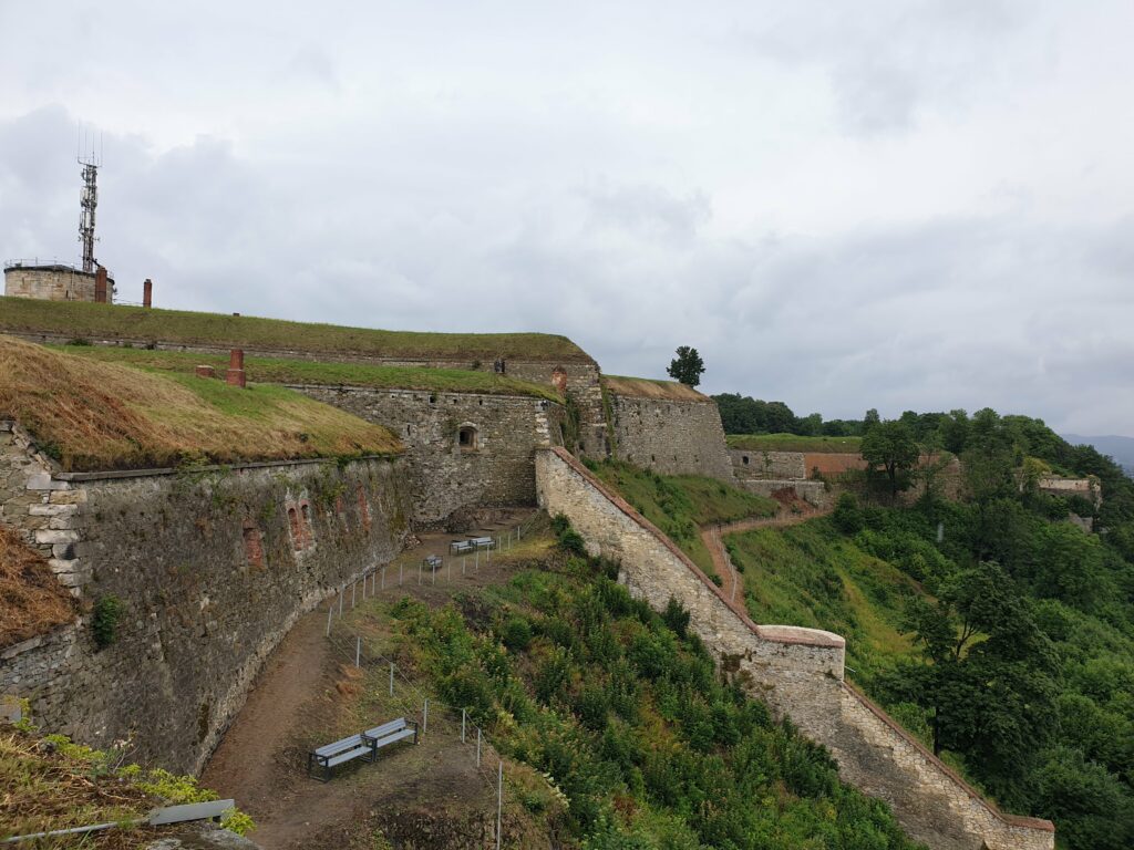 Wielopoziomowe fortyfikacje Twierdzy Kłodzkiej ze ścieżką spacerową i ławkami.