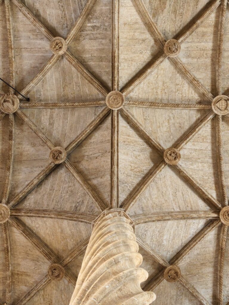 Zbliżenie na misterne, gotyckie sklepienie żebrowe oraz górną część skręconej kamiennej kolumny we wnętrzu Giełdy Jedwabiu w Walencji.