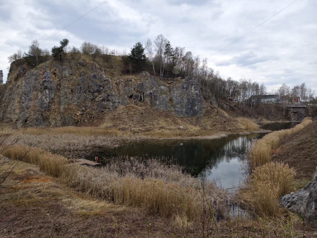 Szmaragdowe jeziorko na dnie dawnego wyrobiska na Kadzielni, w którym odbijają się wysokie, wapienne ściany rezerwatu.