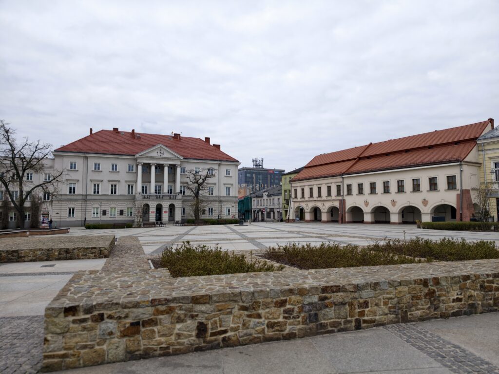 Pochmurny dzień na zrewitalizowanym Rynku w Kielcach z widocznymi zabytkowymi kamienicami i kawiarnianymi ogródkami.