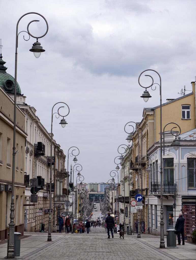 Spacerujący ludzie na reprezentacyjnym deptaku wzdłuż ulicy Sienkiewicza w Kielcach, w otoczeniu odrestaurowanych, zabytkowych kamienic.