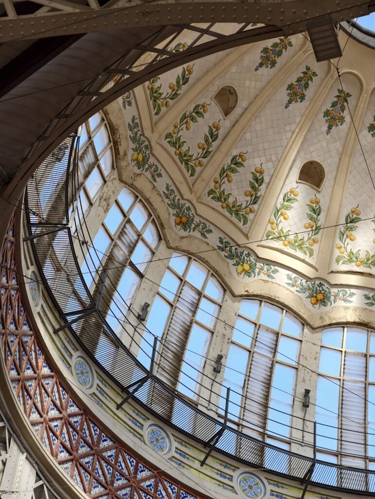 Zbliżenie na imponującą, wielobarwną kopułę ze szkła i kutego żelaza, wpuszczającą naturalne światło do wnętrza hali targowej Mercado Central w Walencji.