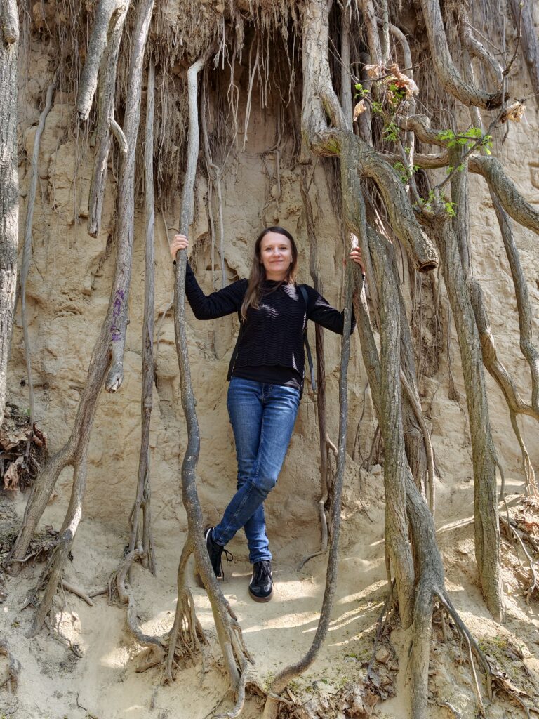Turystka pozująca z potężnymi, obnażonymi korzeniami drzew zwisającymi ze stromych ścian lessowych w Wąwozie Królowej Jadwigi w Sandomierzu.