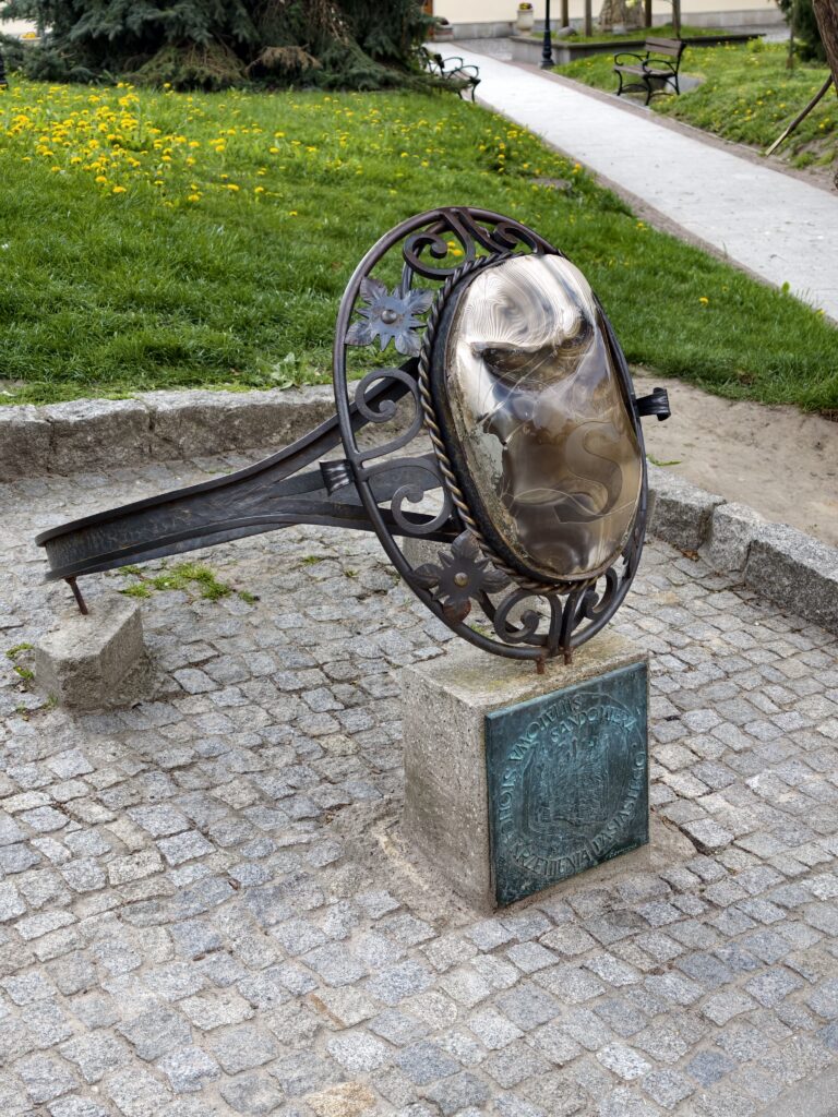 Metalowa rzeźba z bocznej perspektywy w kształcie pierścienia z krzemieniem pasiastym na skwerze w Sandomierzu.