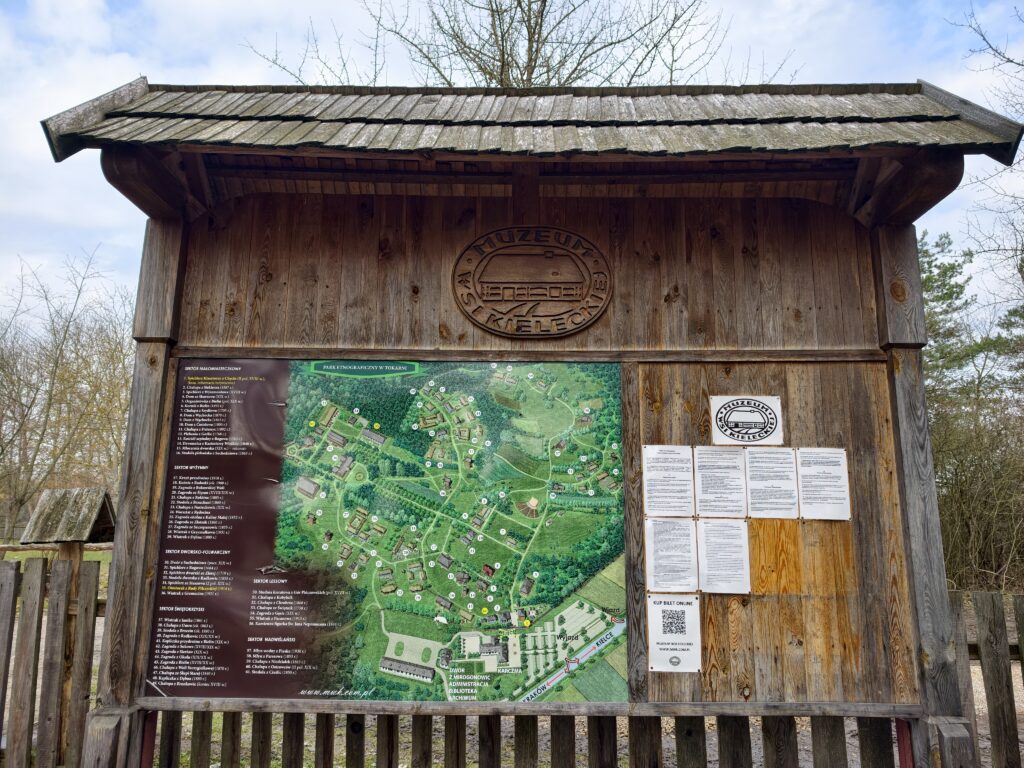 Drewniana tablica informacyjna z planem sytuacyjnym i mapą obiektów Muzeum Wsi Kieleckiej w Tokarni