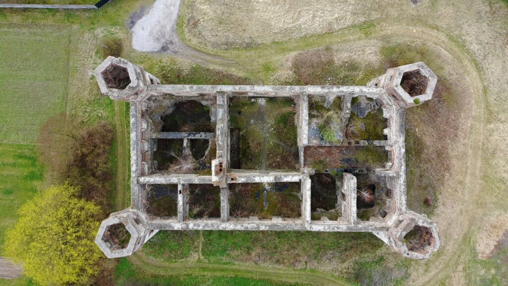 Dokładne zdjęcie z drona (plan lotniczy) pokazujące regularny układ i cztery wieże narożne ruin Pałacu Tarłów w Podzamczu Piekoszowskim.