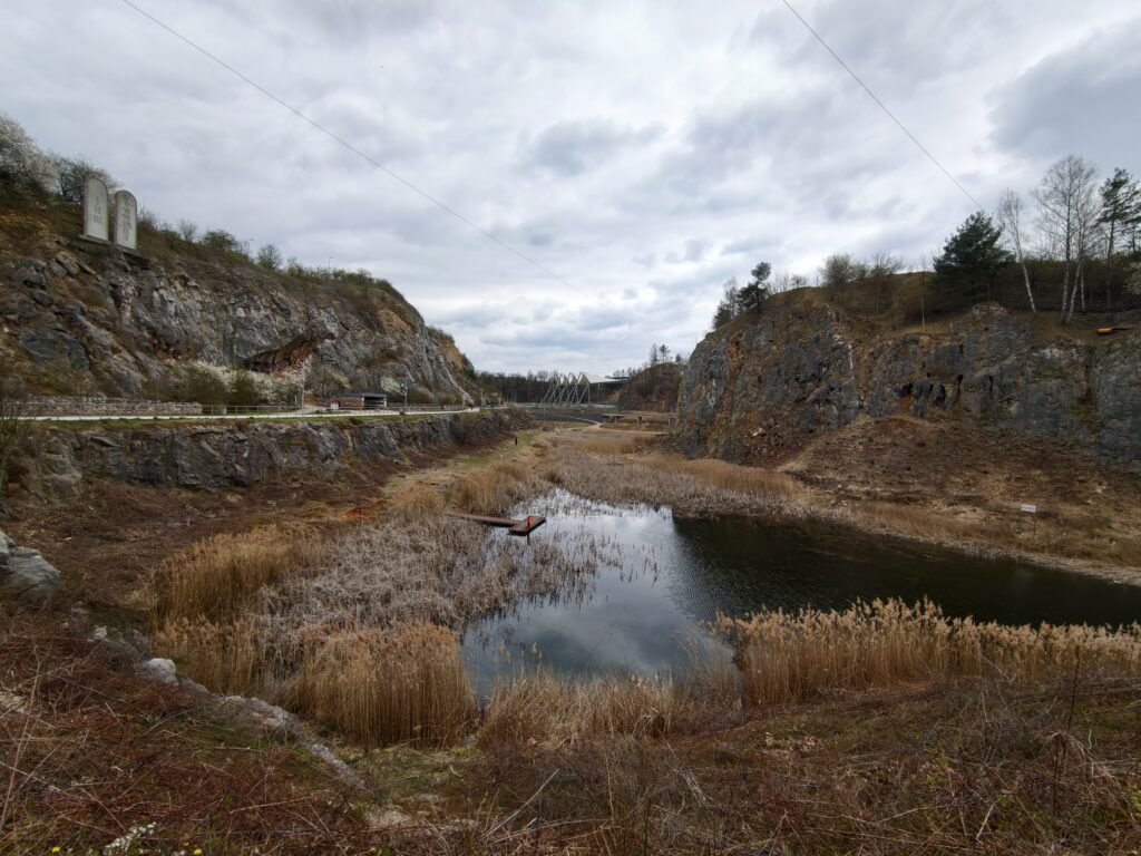 Szeroka panorama rezerwatu Kadzielnia w Kielcach z widocznym w dole jeziorkiem oraz zarysem Gór Świętokrzyskich na horyzoncie.
