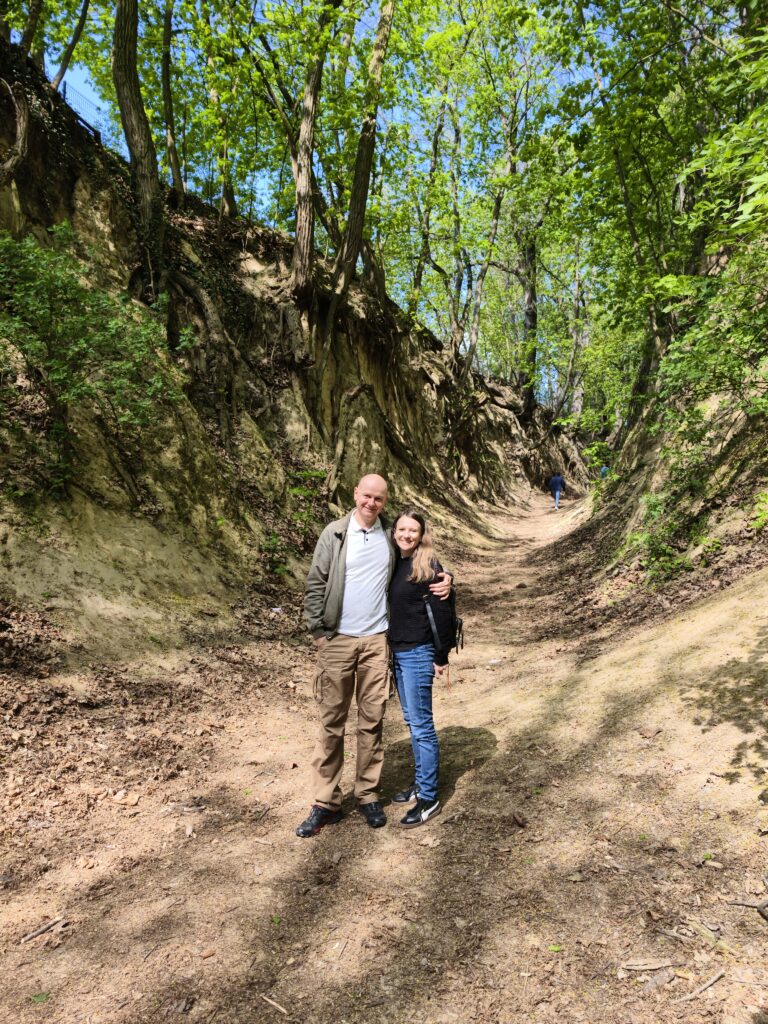 Uśmiechnięta para turystów stojąca na piaszczystym dnie Wąwozu Królowej Jadwigi w Sandomierzu, otoczona stromymi ścianami z lessu.