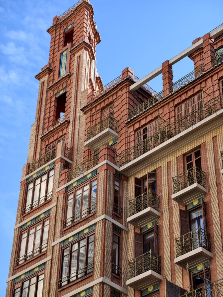 Elegancka, bogato zdobiona fasada historycznej kamienicy w centrum Walencji z kutymi balkonami i rzeźbieniami wokół okien.