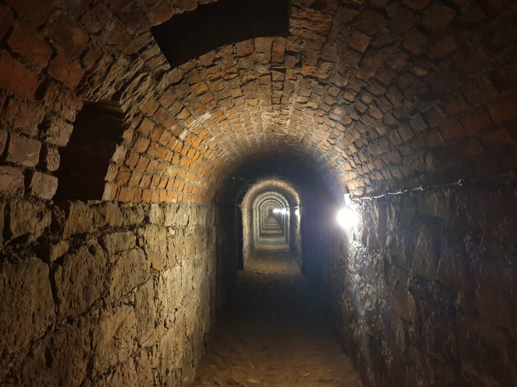 Ciemny korytarz minerski z ceglanym sklepieniem w podziemiach pod kłodzką twierdzą.
