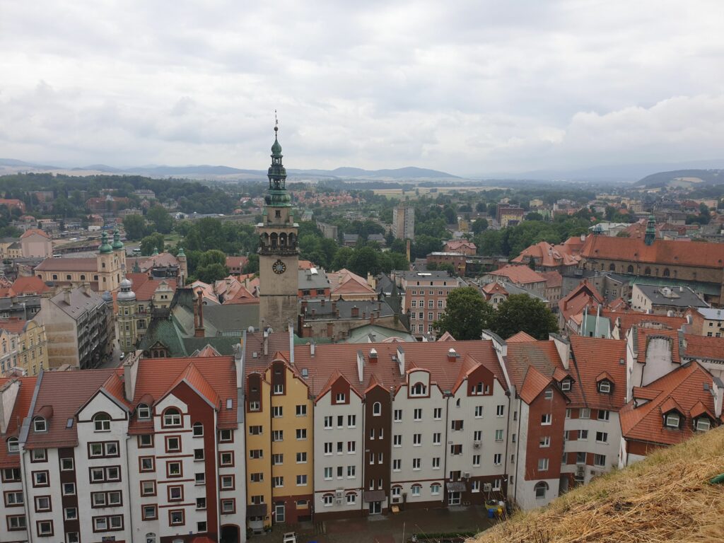 Rozległa panorama z najwyższego bastionu Twierdzy Kłodzkiej na zabytkowe dachy miasta i okoliczne pasma górskie.