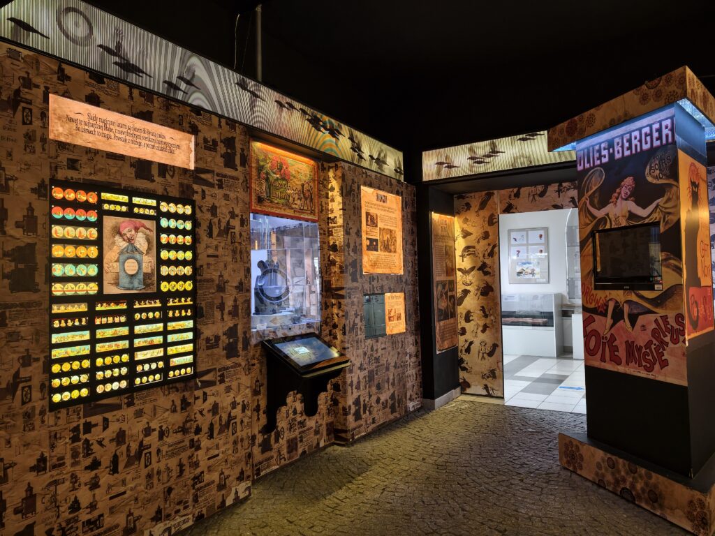 Zaciemniona sala wystawowa w kieleckim muzeum z wyeksponowanymi starymi rzutnikami do slajdów, w tym kultowym projektorem Ania, wyświetlającymi obraz na ścianie.