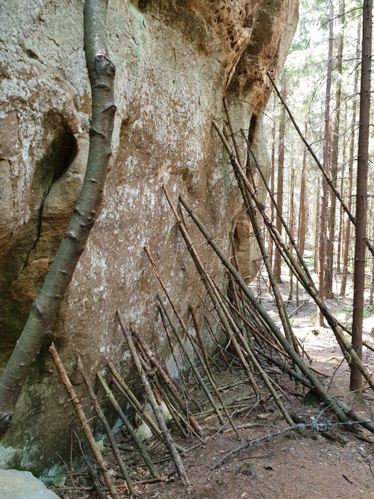 Zbliżenie na podstawę formacji Skalny Grzyb, gdzie turyści ułożyli dziesiątki małych patyków, symbolicznie "podtrzymujących" skałę.
