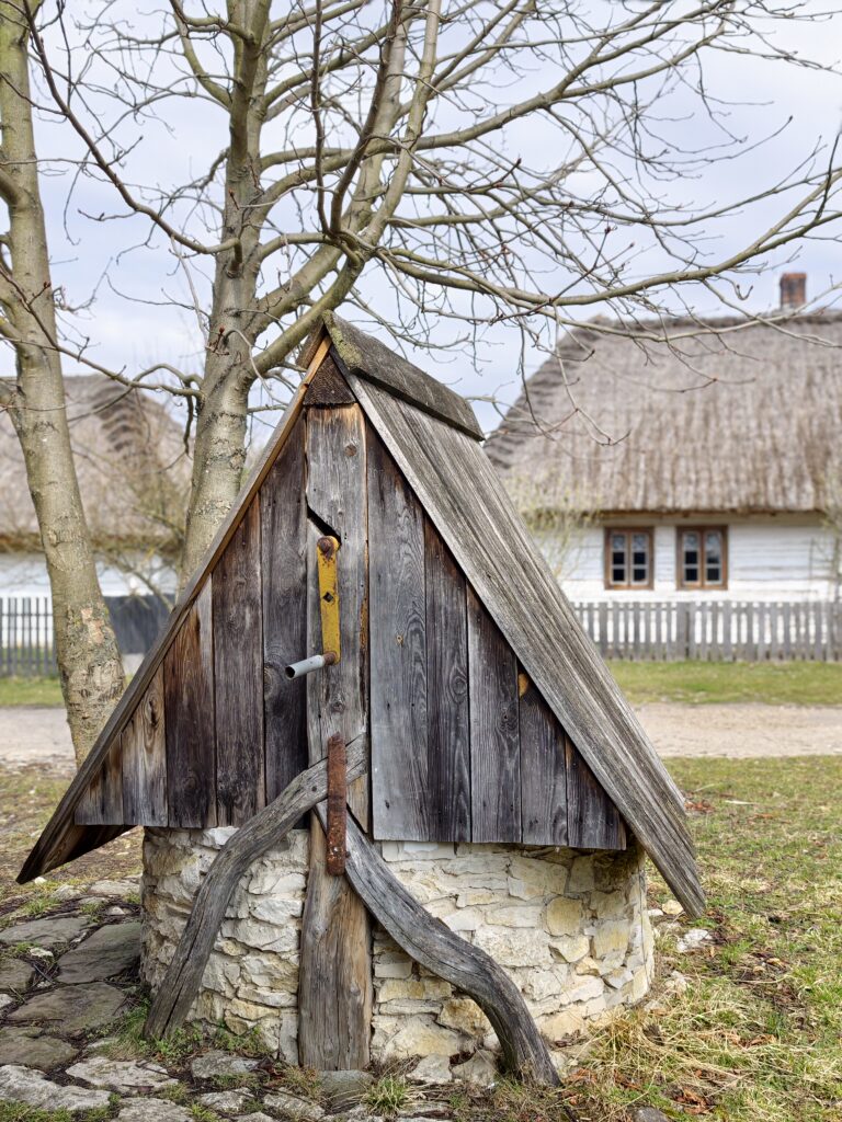 Tradycyjna drewniana studnia z żurawiem na środku wiejskiego podwórka w Muzeum Wsi Kieleckiej