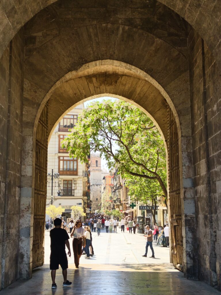 Zbliżenie na masywne, okute drewniane wrota i gruby, kamienny łuk gotycki stanowiący główne wejście do wież Torres de Serranos w Walencji.
