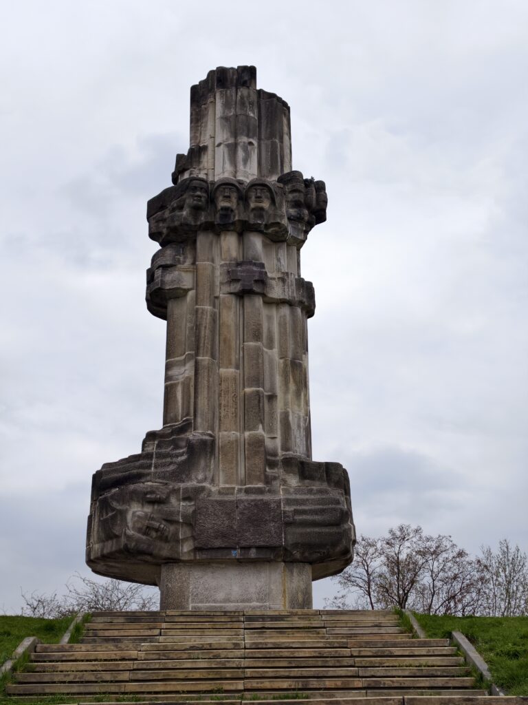 Potężny, betonowy Pomnik Bojowników o Wyzwolenie na Wzgórzu Harcerskim, górujący nad rezerwatem na tle panoramy Kielc.