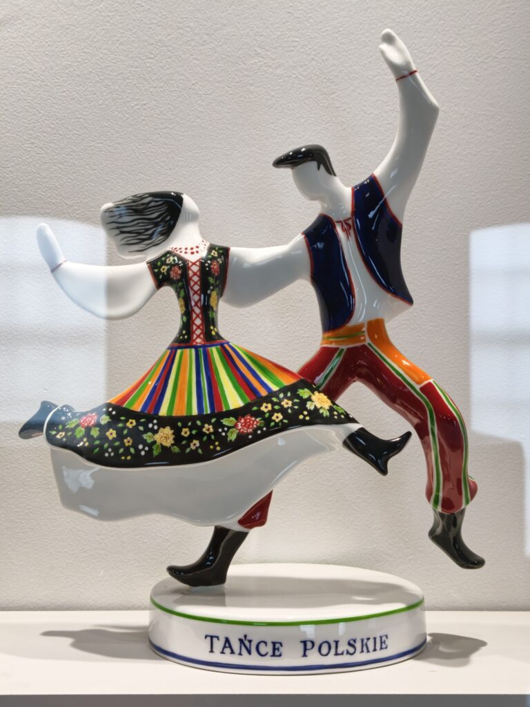 Kolorowa, błyszcząca figurka porcelanowa przedstawiająca parę w tradycyjnych strojach ludowych z napisem Tańce Polskie, w Ćmielowie.