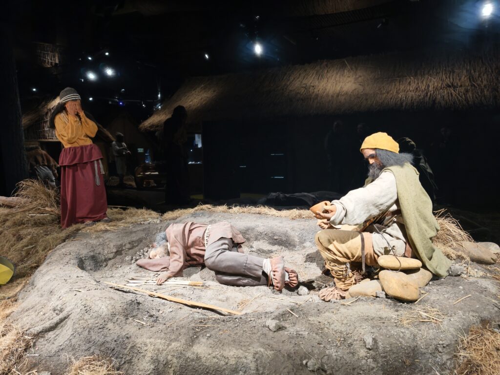Diorama w muzeum Krzemionki Opatowskie z figurami ludzi epoki neolitu krzeszących ogień przy ognisku w osadzie pradziejowej