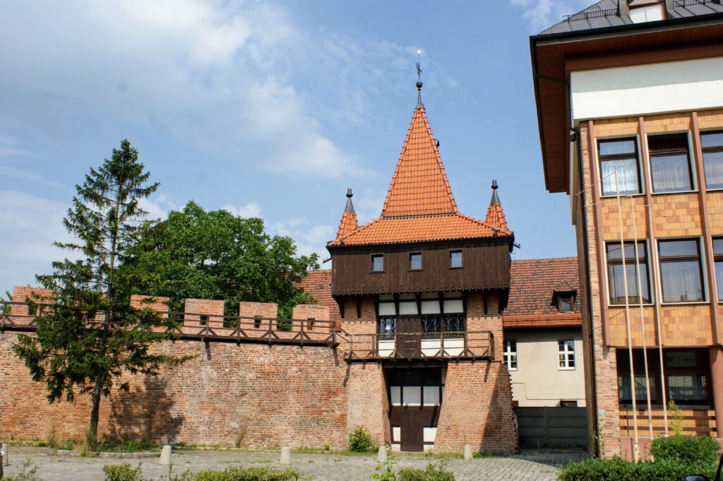 Zabytkowe ceglane mury obronne Opola z drewnianym gankiem i basztą o czerwonym dachu