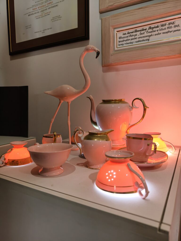 Podświetlona ekspozycja unikalnej różowej porcelany w Ćmielowie, w tym dzbanek, filiżanki i figurka flaminga.