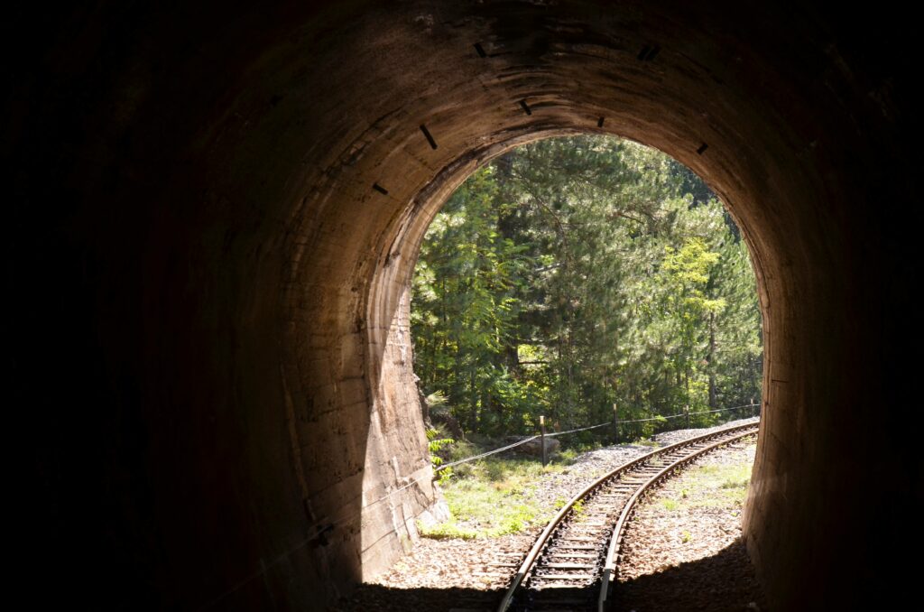 Widok z wnętrza ciemnego tunelu Szargańskiej Ósemki na rozświetlone słońcem tory i sosnowy las