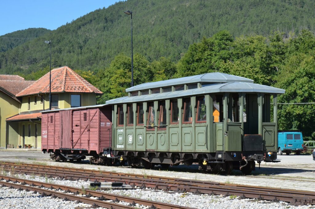 Zabytkowy zielony wagon osobowy i bordowy wagon towarowy Szargańskiej Ósemki przy stacyjnym budynku w Mokrej Górze