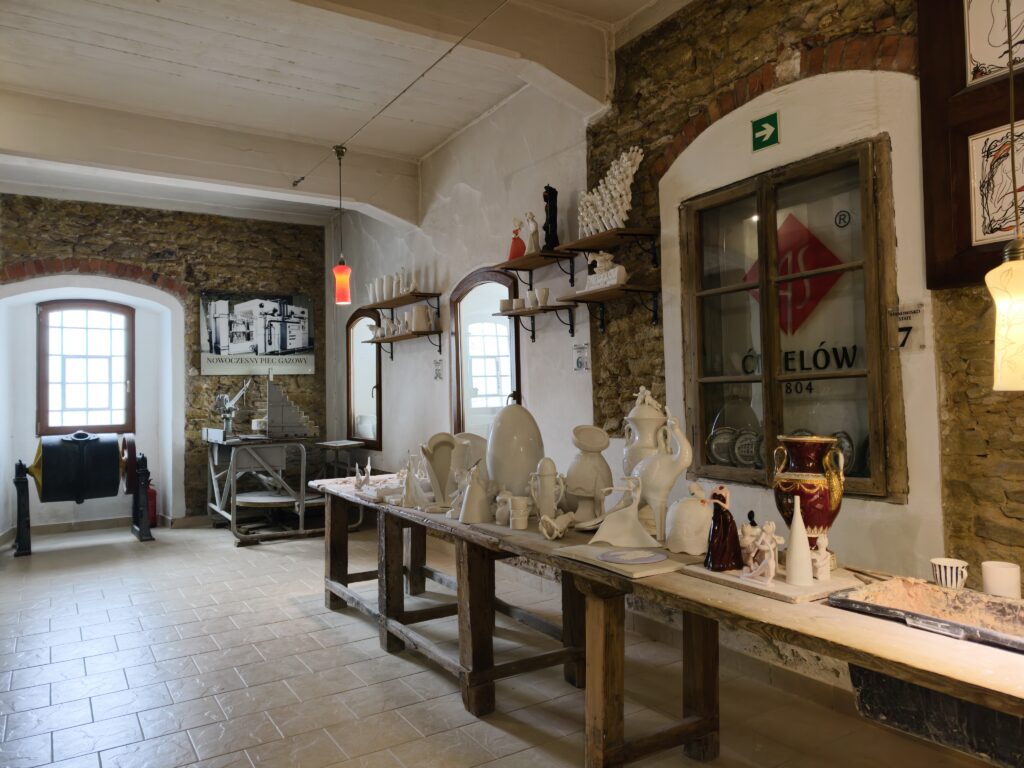 Pomieszczenie warsztatowe w Żywym Muzeum Porcelany w Ćmielowie z długim stołem i białymi, nieszkliwionymi formami ceramicznymi.