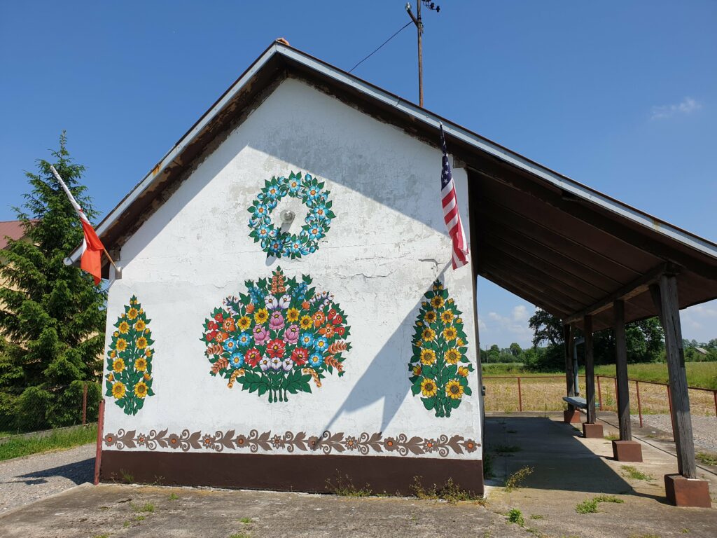 Boczna ściana remizy w Zalipiu z wielkim malowanym bukietem polnych kwiatów, słonecznikami i polską oraz amerykańską flagą.
