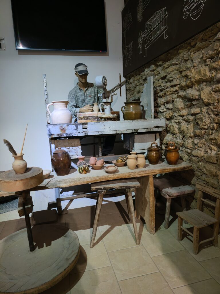 Ekspozycja w muzeum w Ćmielowie przedstawiająca tradycyjne stanowisko garncarskie z manekinem rzemieślnika i glinianymi naczyniami.