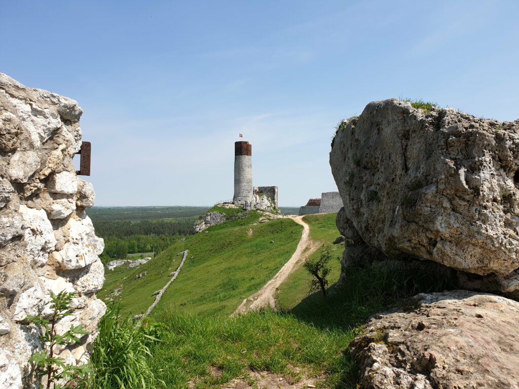 Wieża zamku w Olsztynie widziana zza wapiennych skał, ścieżka prowadząca przez wzgórze na Szlaku Orlich Gniazd