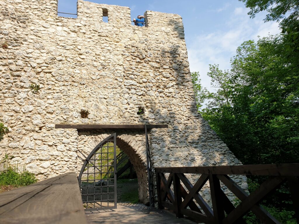 Brama wjazdowa zamku Pilcza w Smoleniu z metalową kratą i drewnianym mostem