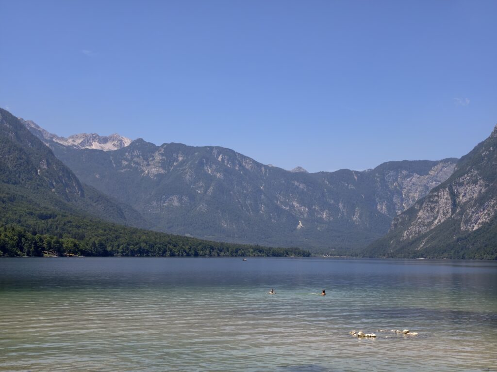Osoby pływające w jeziorze Bohinj na tle szczytów Alp Julijskich