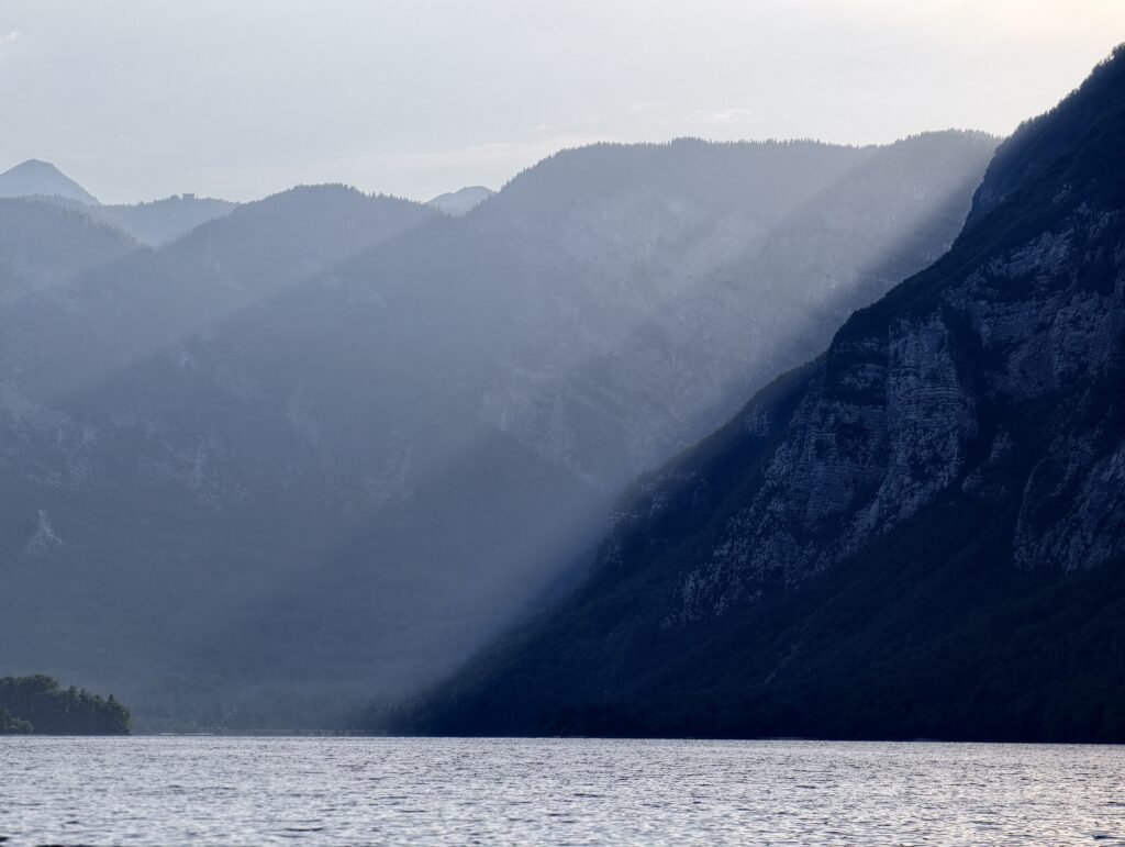 Promienie słońca przebijające się przez góry nad jeziorem Bohinj