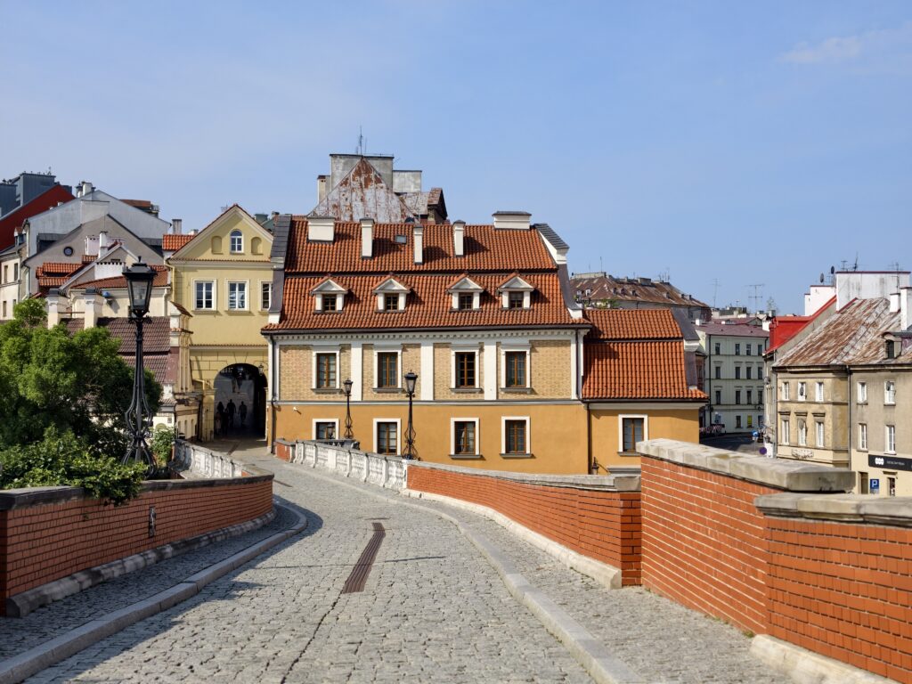 Brukowana droga prowadząca przez most w kierunku Bramy Grodzkiej, otoczona zabytkowymi kamienicami Starego Miasta w Lublinie