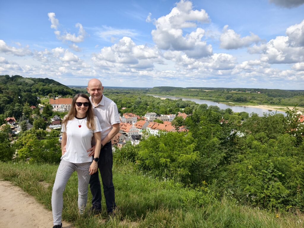 Turyści pozujący do zdjęcia na tle panoramy Kazimierza Dolnego i rzeki Wisły ze szczytu Góry Trzech Krzyży