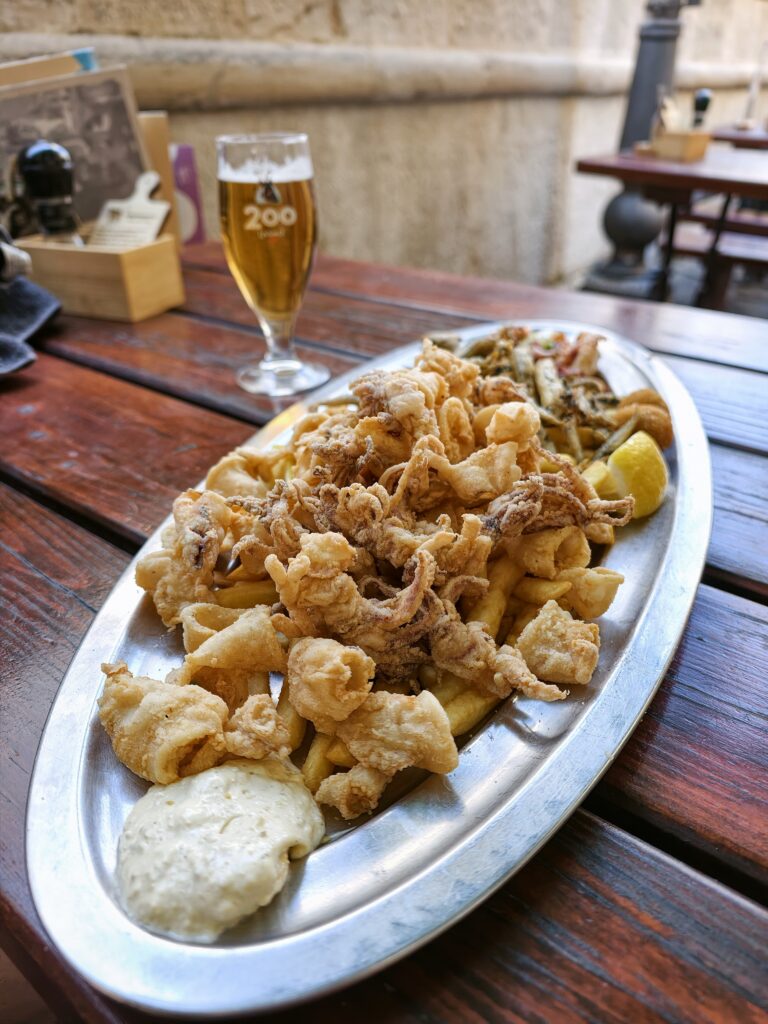 Duży metalowy talerz pełen smażonych owoców morza, kalmarów i frytek podany w restauracji w Piranie.