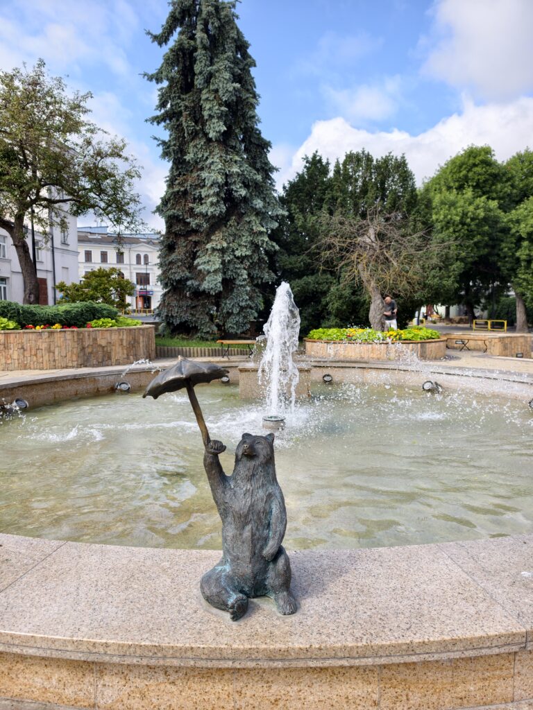 Brązowa figura misia z parasolką siedzącego przy fontannie w centrum Chełma