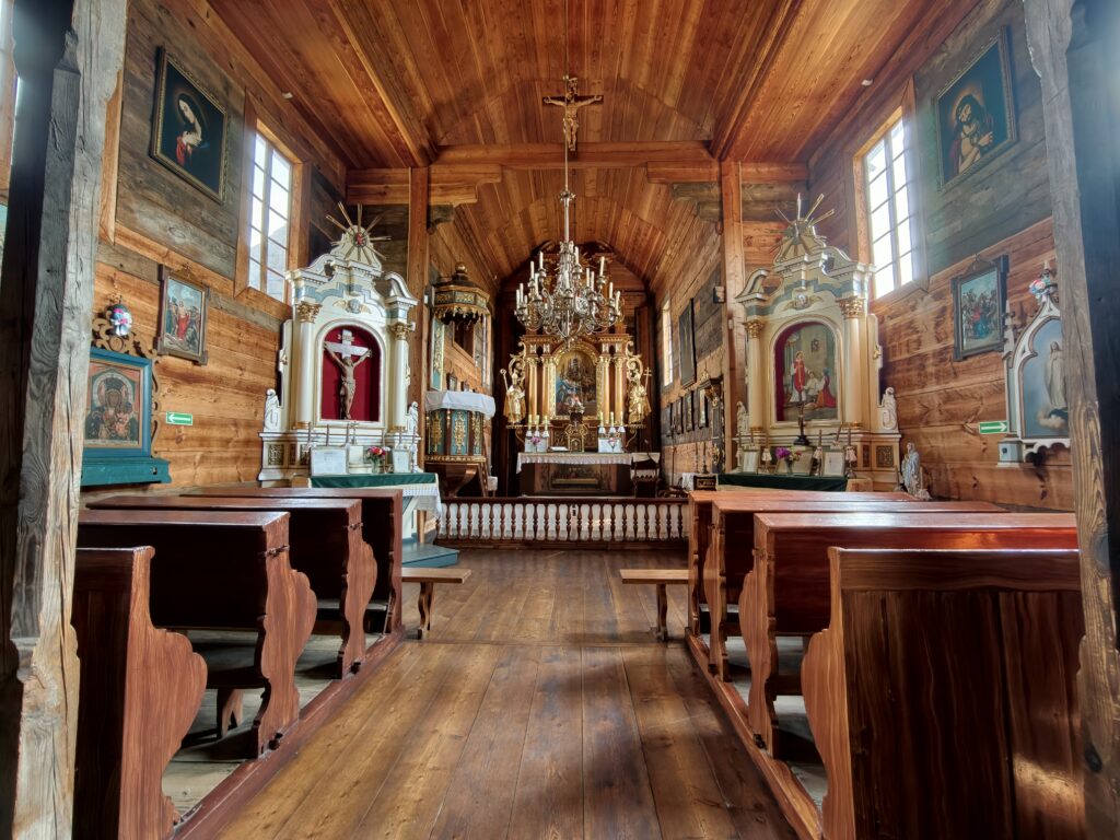 Wnętrze drewnianej cerkwi w Muzeum Wsi Lubelskiej z bogato zdobionym ołtarzem, żyrandolem i rzędami ław