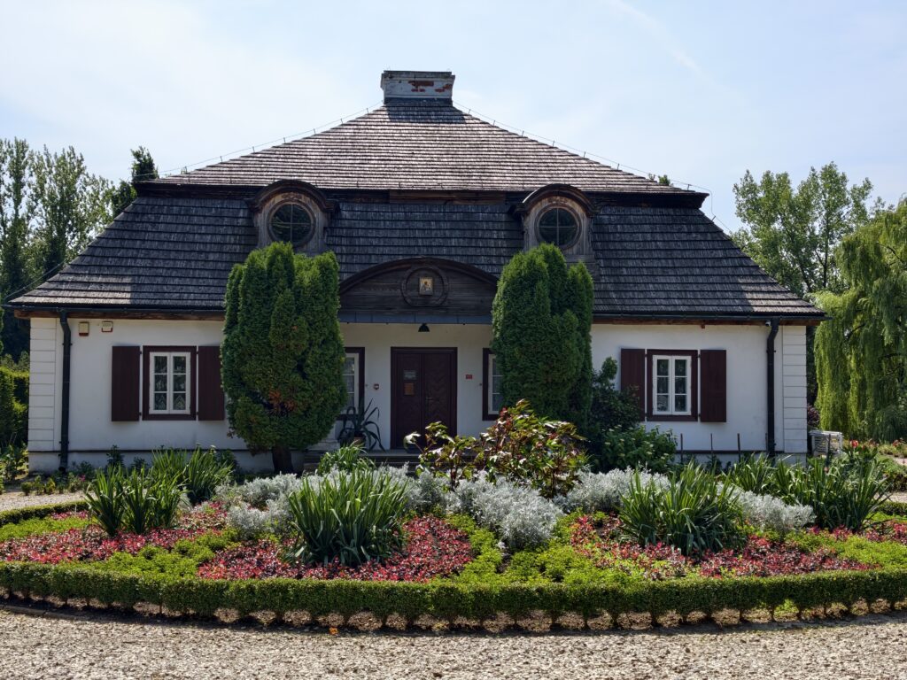 Zabytkowy, kryty gontem dworek w Muzeum Wsi Lubelskiej (skansenie) otoczony ogrodem kwiatowym